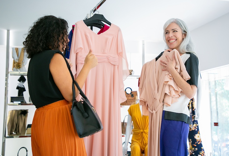 Pic for Clothing Swap Event - Cheerful woman showing chosen dress with hanger to her friend and laughing. Two ladies shopping in fashion store together. Consumerism or shopping concept